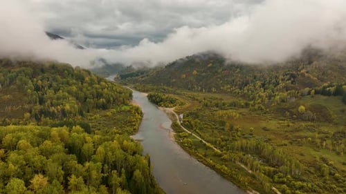 Aerial view of a winding river and dense autumn forest with a small village