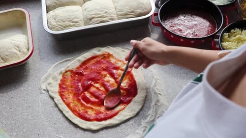 Frau macht zu Hause Pizza und verteilt Tomatensauce auf Pizzateig mit einer Kelle in 4K