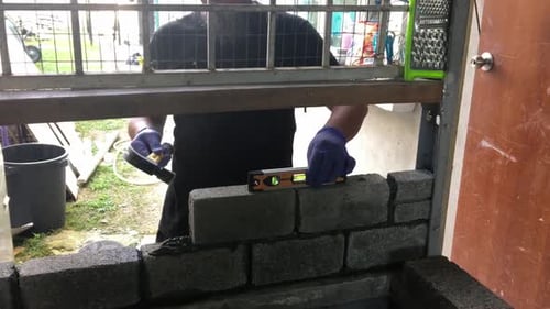 Adult male craftsman's hands with purple latex gloves tampers cement stone bricks with hammer and ch