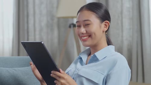 Close Up Of Asian Woman Enjoys Using A Tablet While Lying On Sofa In The Living Room