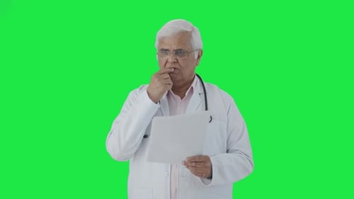 Confused Indian senior doctor reading reports Green screen