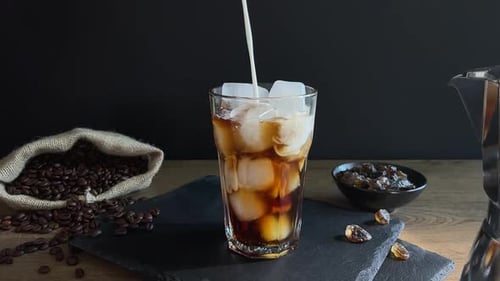 Pouring Milk Into Glass of Coffee and Ice