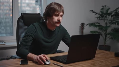 Man Seated at Table Using Laptop Computer in Office Setting