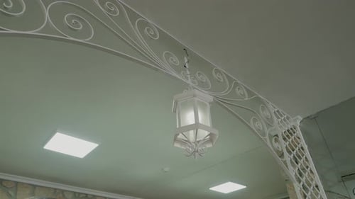 white hanging lantern under a decorative metal archway with swirl patterns indoors