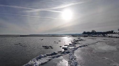 Cinematic drone view of the frozen Baltic Sea coastline during winter at sunset. The aerial