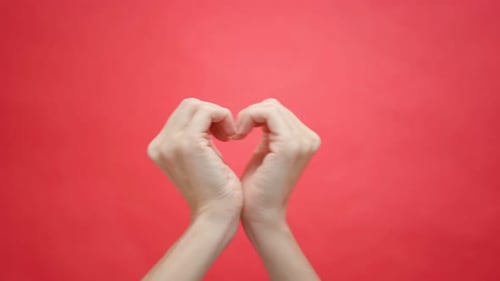 Hands Forming Heart Symbol on Red Background