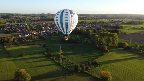 Hot air balloon flying above rural landscape near small town, aerial orbit view