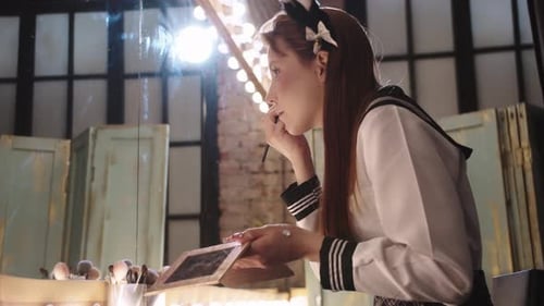 Cute Young Woman in School Uniform Doing Eye Makeup Sitting at the Backstage