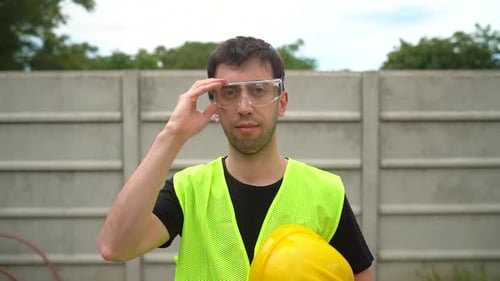 A Construction Worker, Holding His Yellow Hard Hat, Removes His Standard Safety Spectacles - Medium