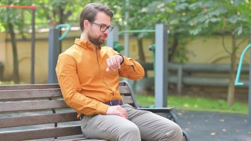 Man Checking Smartwatch While Sitting on Park Bench