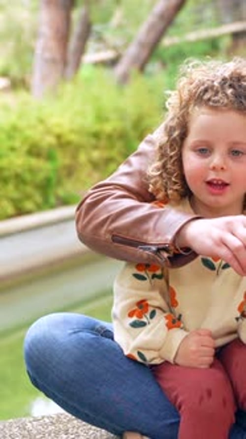 Curious Girl Blowing Bubbles Outdoors Sitting with Her Mother