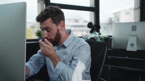 Man Blowing Nose While Working at Computer