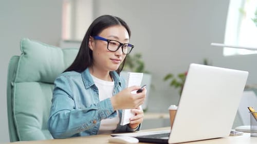 Woman in Video Call Taking Notes at Desk