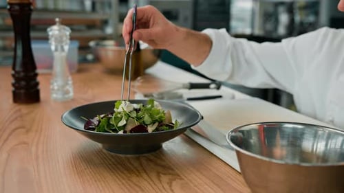 Professional kitchen chef puts salad leaves with pear and cheese on a plate with tongs ingredients