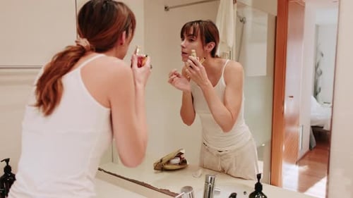 Woman Applying Lotion and Facial Roller in Bathroom