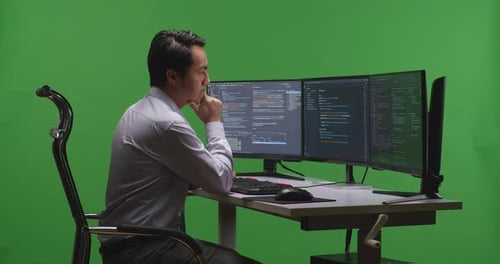 Asian Man Developer Thinking While Write Code With Multiple Computer Screens In Green Screen Studio