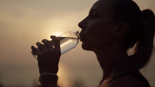Woman Drinks Water at Sunset