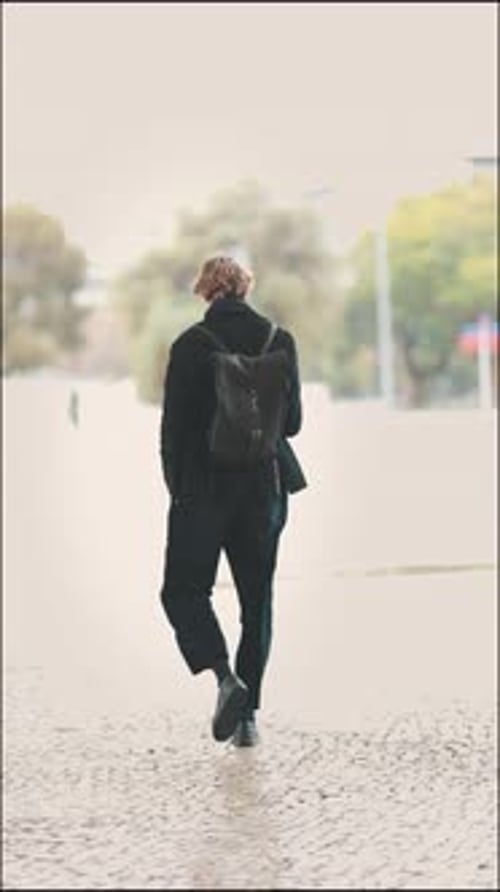 Stylish Young Man Walking on Wet Cobblestone Street