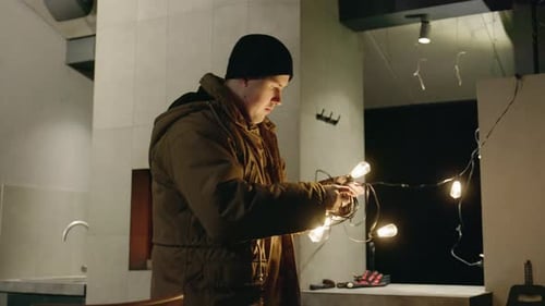 Man Untangling Christmas Lights Indoors at Night