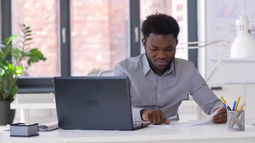 African american businessman working with laptop and financial papers at his office