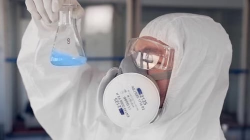 Scientist in Protective Suit Swirling Blue Liquid in Flask