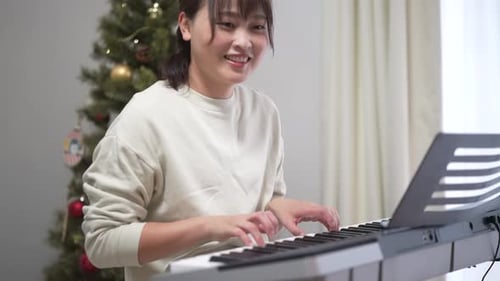 Woman Plays Piano Next to Christmas Tree