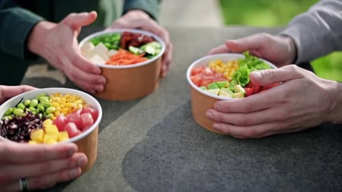 Close view of people placing three poke bowls with vegetables, fruits, fish and seaweed salad on a t
