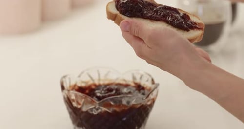 Mão feminina espalhando geléia em fatia de pão