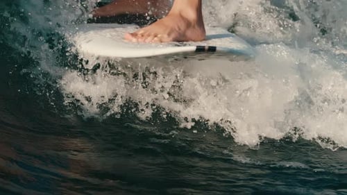 Close up of surfer's feet on surfboard gliding through water and wave in slow motion