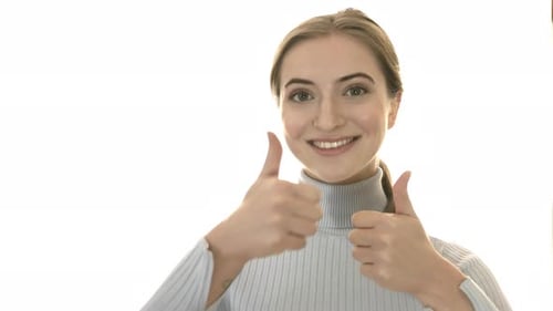 Smiling young woman in studio on white background shows thumbs up.