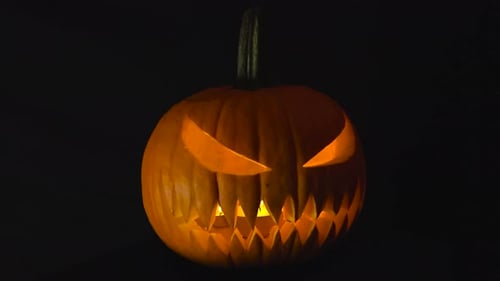 Scary orange and carved halloween pumpkin with candles burning inside. Black studio background.