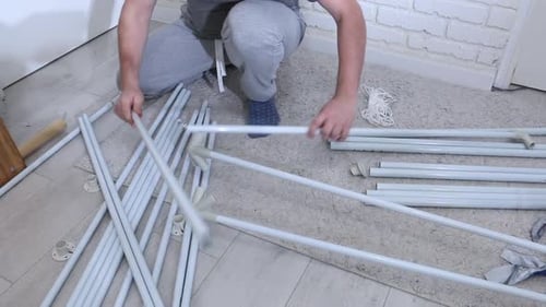 Un homme assemble une tente de jardin. Les pièces à assembler sont disposées sur le sol