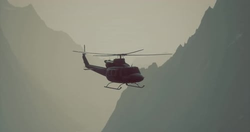 Helicopter Flying Through Mountain Range at Dusk with Misty Backdrop