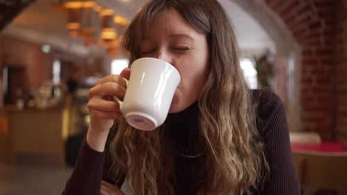 Woman Enjoying a Hot Beverage in a Cozy Cafe