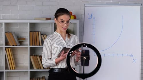 Female Teacher in Glasses Holding Tablet and Marker Showing Information on Flipchart Board and