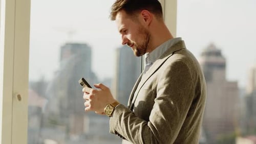Young Adult Using Smartphone By Window in Urban Setting