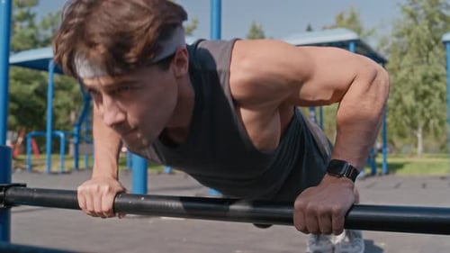 Doing Push ups on Metallic Bar over Ground during Outdoor Workout Session