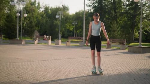Young Lady Skating in Park Surrounded By Greenery and Benches on Sunny Day