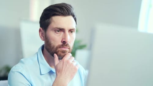 Portrait close up of pensive thinking handsome bearded man in front of laptop computer monitor