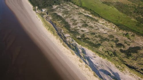 A remote coastline with sandy beach and lush green dunes, aerial view