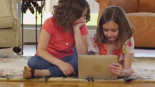 Two Girls Using Tablet Device Together on Rug
