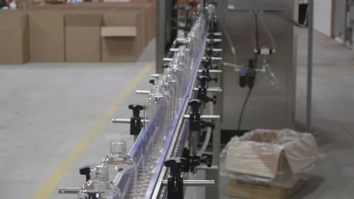Les bouteilles en plastique se déplacent en ligne sur une pièce d'équipement robotique. Des boîtes en papier se trouvent à l'arrière-plan.
