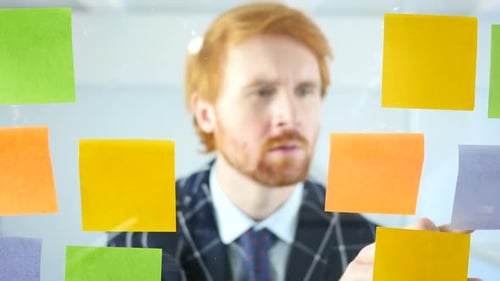 Businessman Working On Sticky Notes Attached on Glass in Office