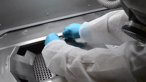 Laborant in weißem Schutzanzug und Handschuhen installiert eine Metallplattform