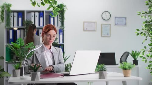 Jeune femme travaillant sur ordinateur et prenant des documents de sa collègue pendant la journée de travail