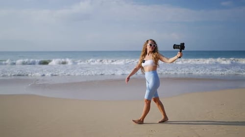 Female Travel Influencer Records on Pro Camera with Wireless Lav Mic on Sandy Beach Curlyhaired