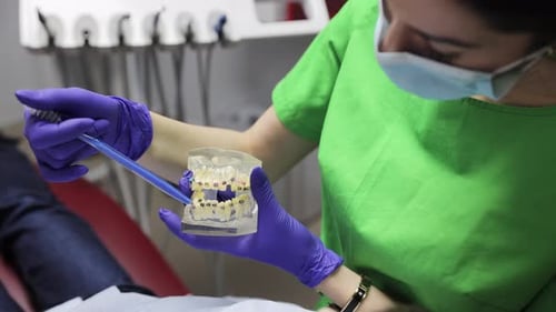 El dentista explica la terapia de ortodoncia a un paciente con un modelo de prótesis dental y soportes