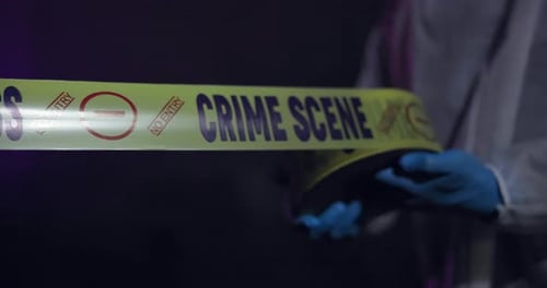 Crime Scene Tape Held by Gloved Hand at Night