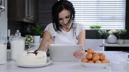 Attractive brunette woman enjoying tablet computer while baking cupcakes at home