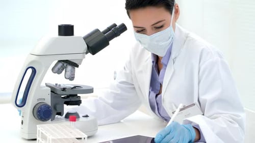 Woman Using Microscope and Tablet in Lab
